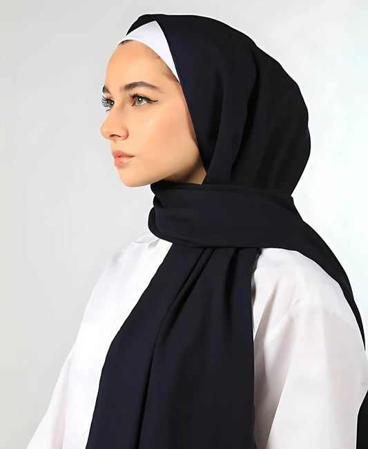 Woman wearing a black hijab and white shirt against a plain background