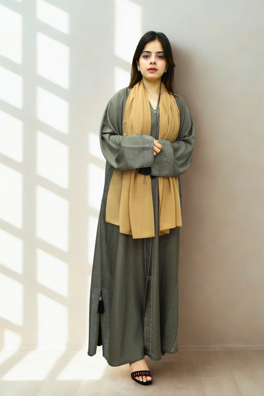 A Girl wearing a Abaya and scarf against a textured wall with sunlight casting shadows.
