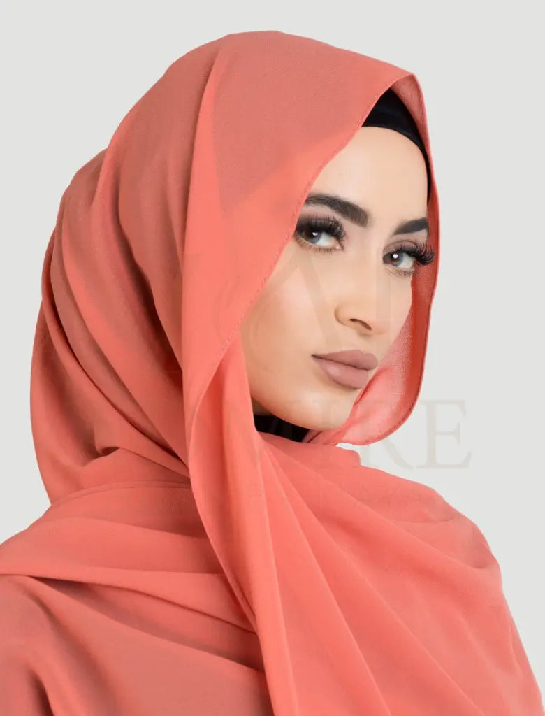 Woman wearing a coral hijab against a plain background