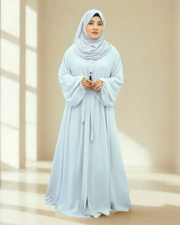 Woman wearing a light blue hijab and abaya in a bright room with natural light.