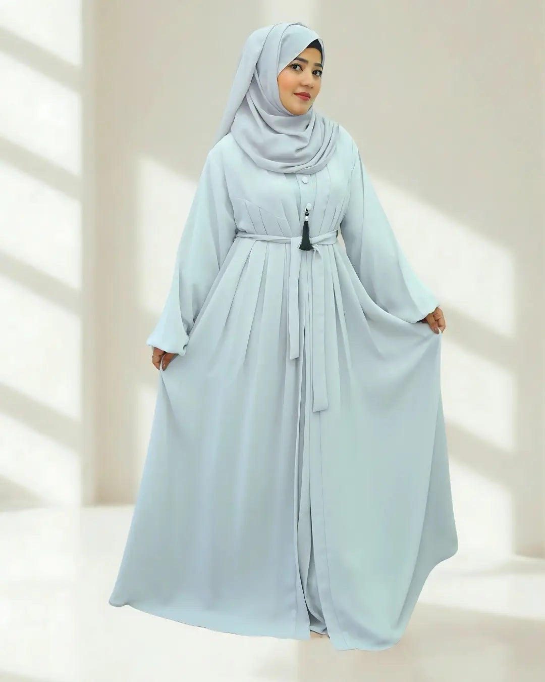 Woman wearing a light blue hijab and abaya against a neutral background