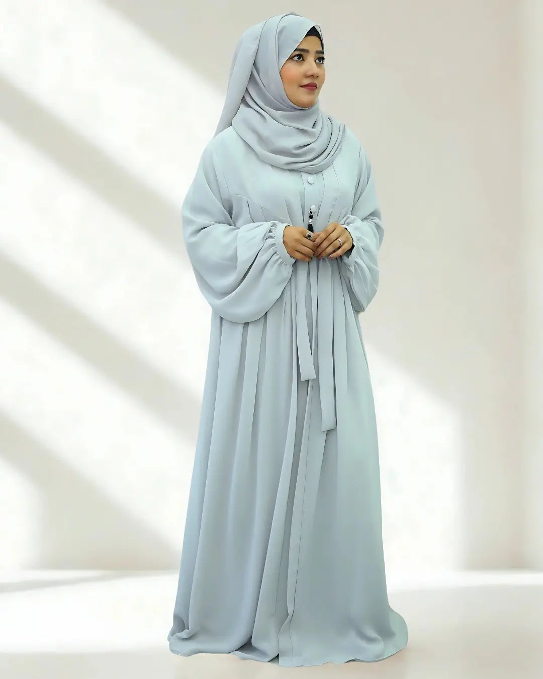 Woman wearing a light blue abaya and hijab on a white background