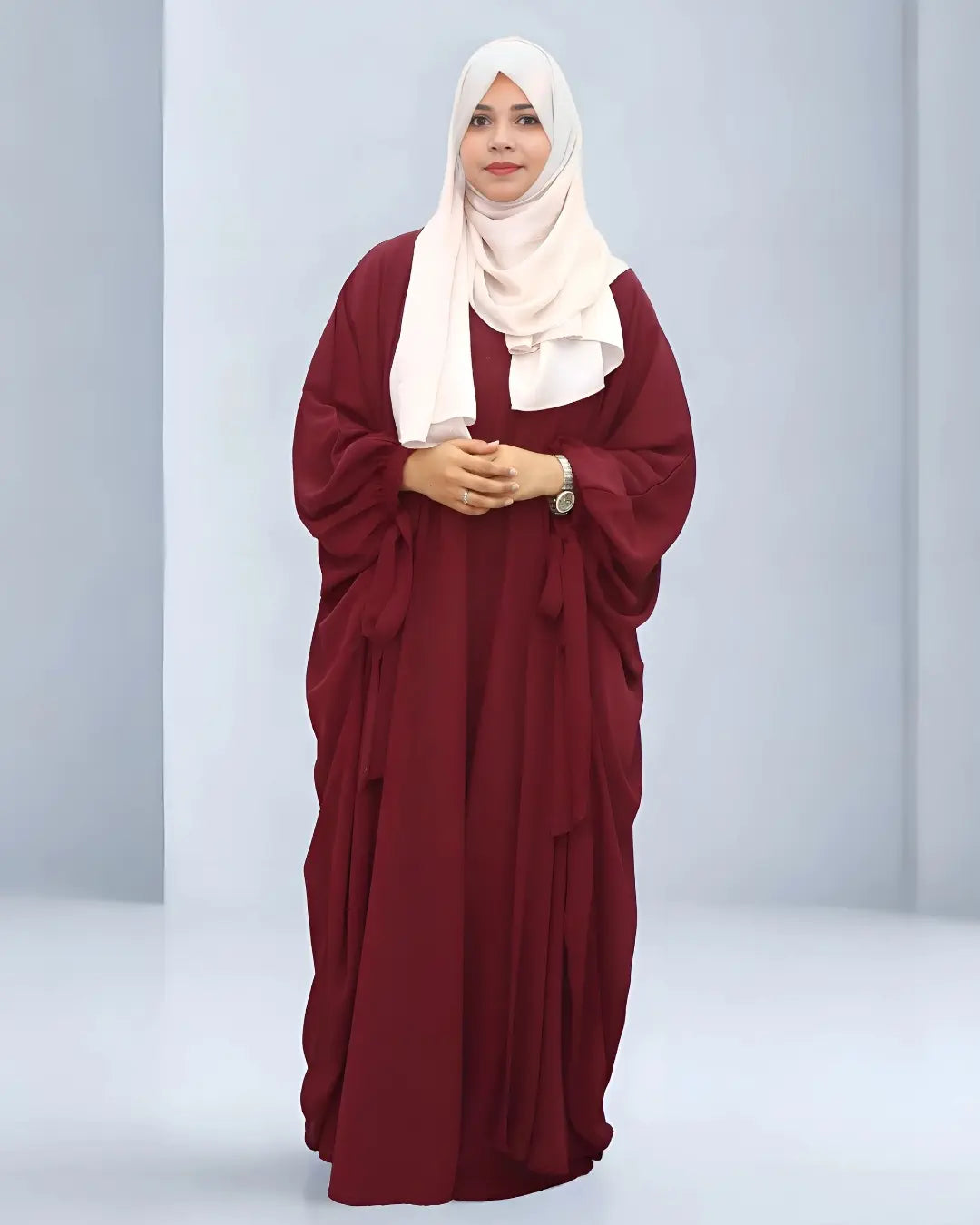 Woman wearing a butterfly abaya with a white hijab on a light gray background