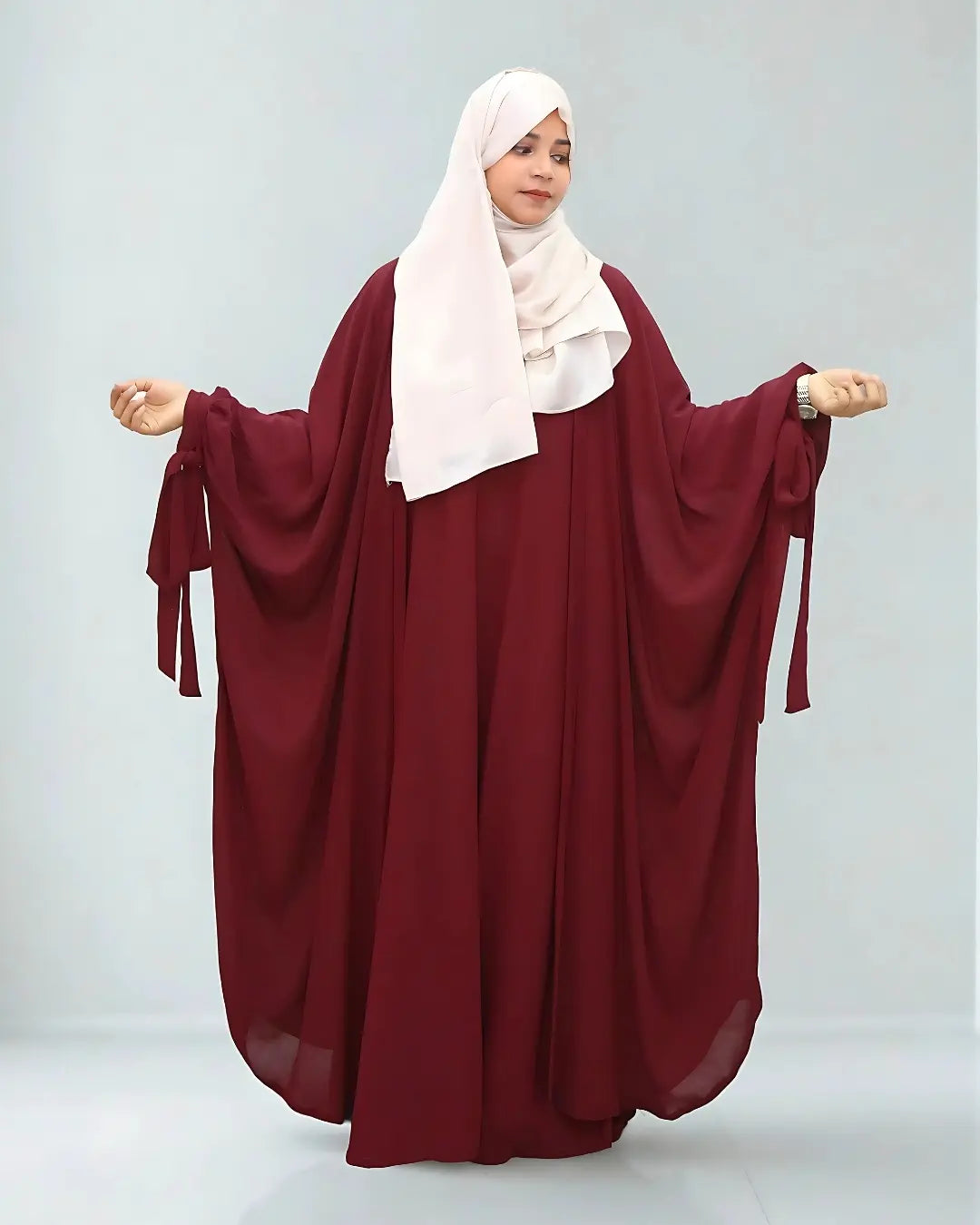 Woman wearing a butterfly abaya with a white hijab on a light gray background
