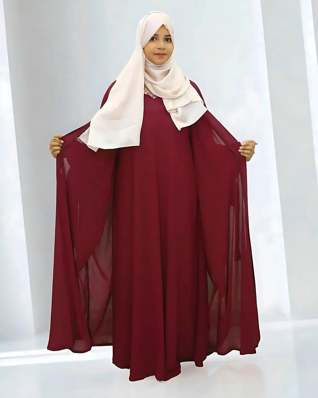 Woman wearing a burgundy abaya and white hijab against a white background