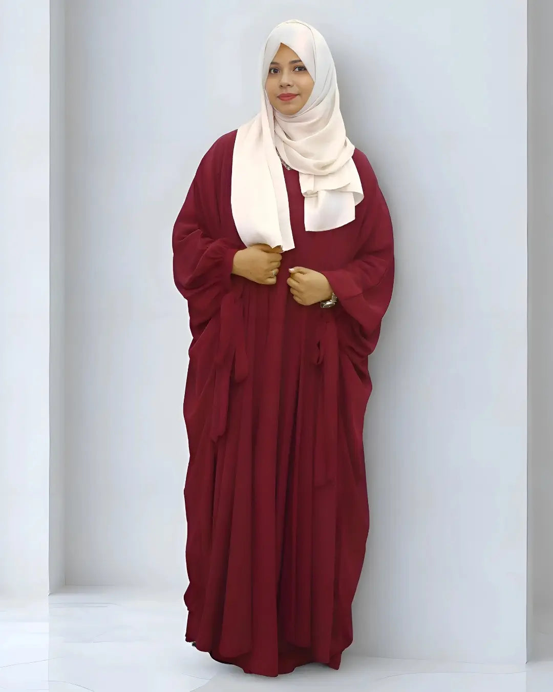 Woman wearing a burgundy abaya and white hijab against a white background
