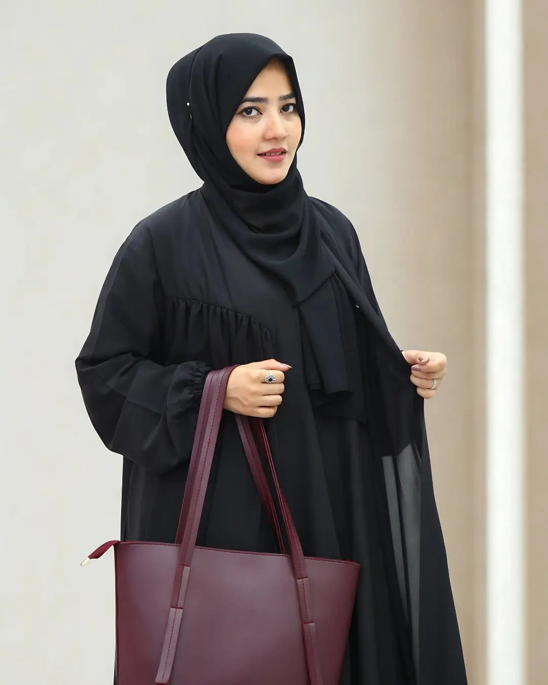 Woman in a black abaya holding a purple handbag against a beige background