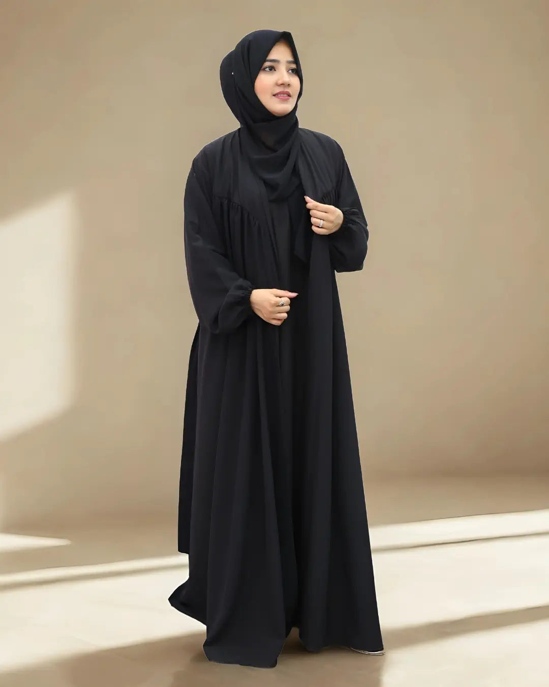 Woman in a black abaya holding a purple handbag against a beige background