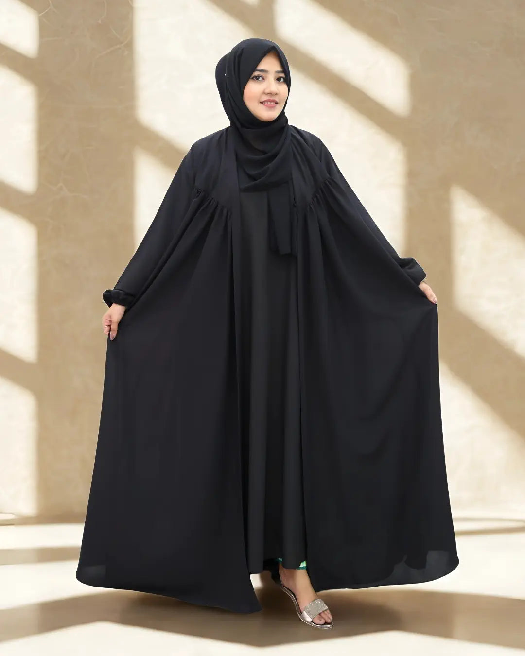 Woman wearing a black abaya in a well-lit room with shadows on the wall.