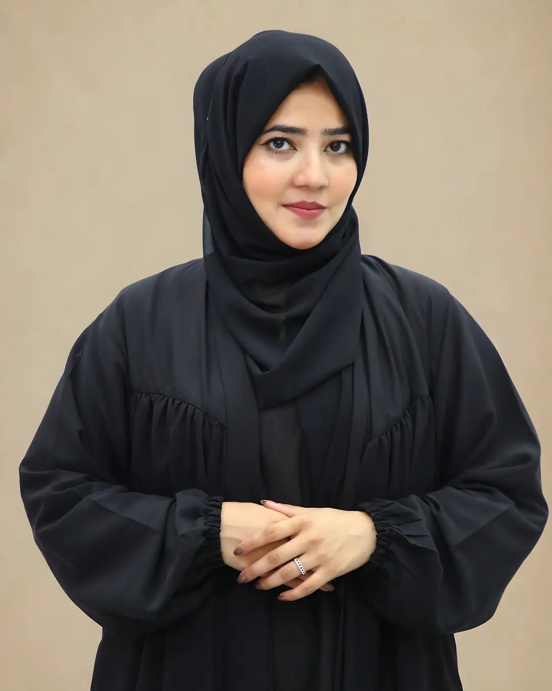 Woman wearing a black hijab and black outfit against a beige background