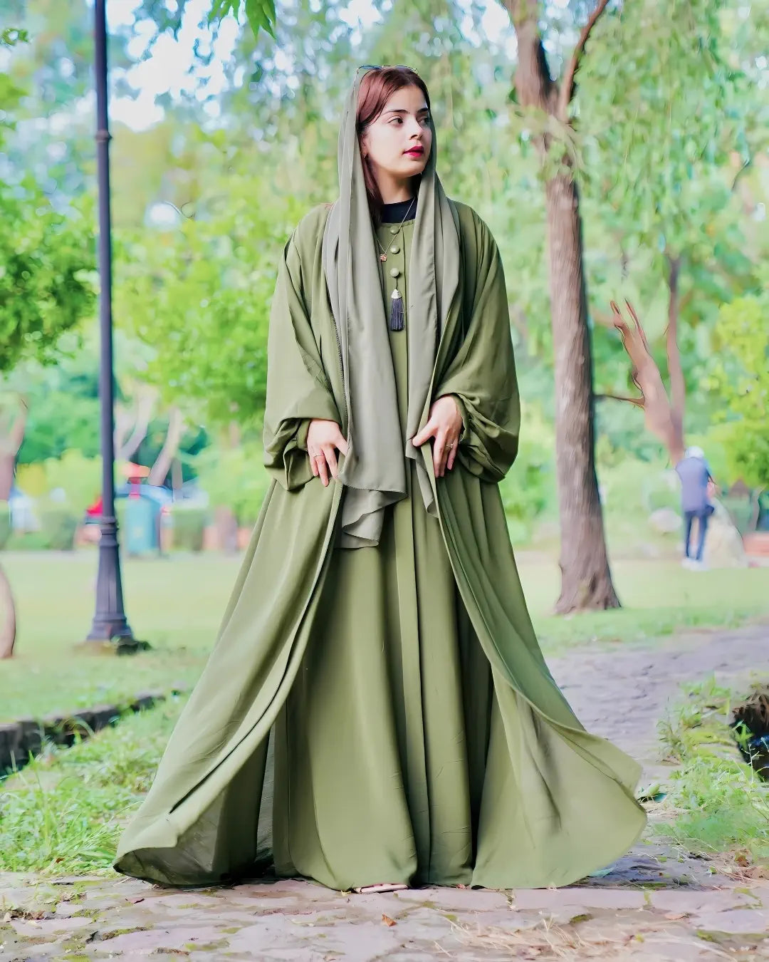 Woman in a long green abaya standing in a park