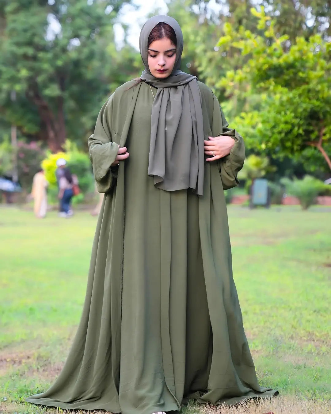 Woman wearing a long green abaya with a hood in an outdoor setting