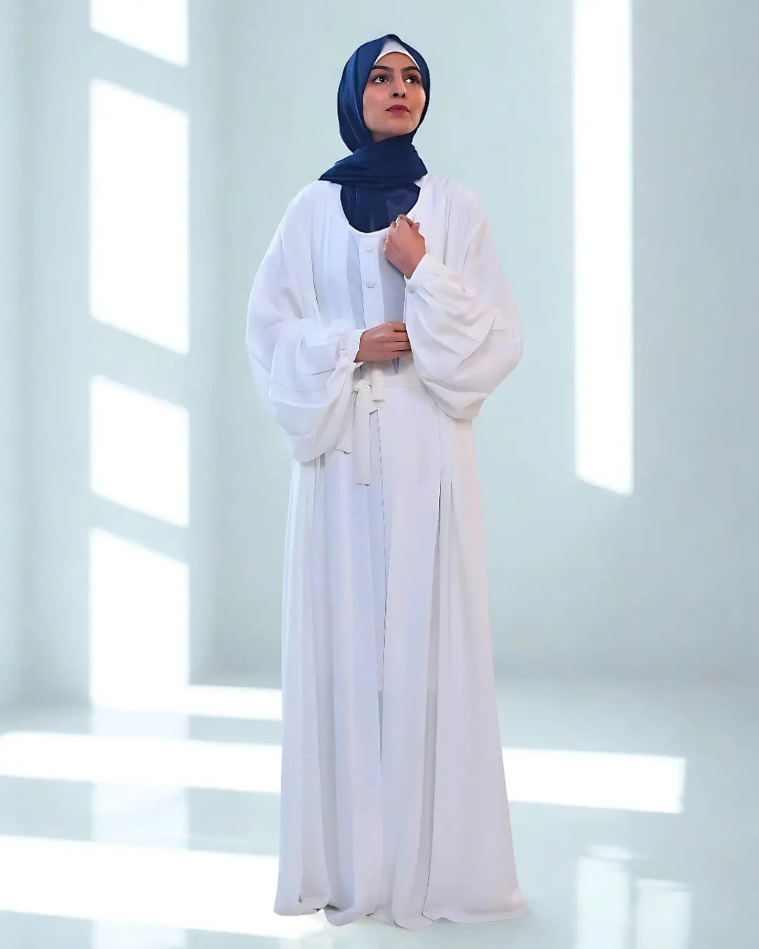 Woman wearing a white abaya with a blue hijab in a bright room