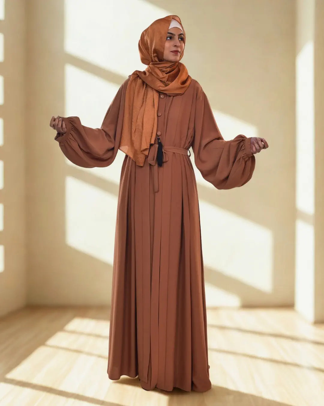 Woman wearing a long brown abaya and hijab in a bright room.