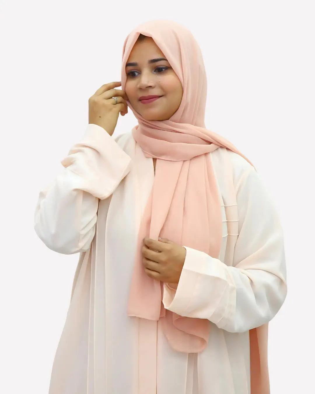 Woman wearing a light pink hijab and white abaya against a plain background