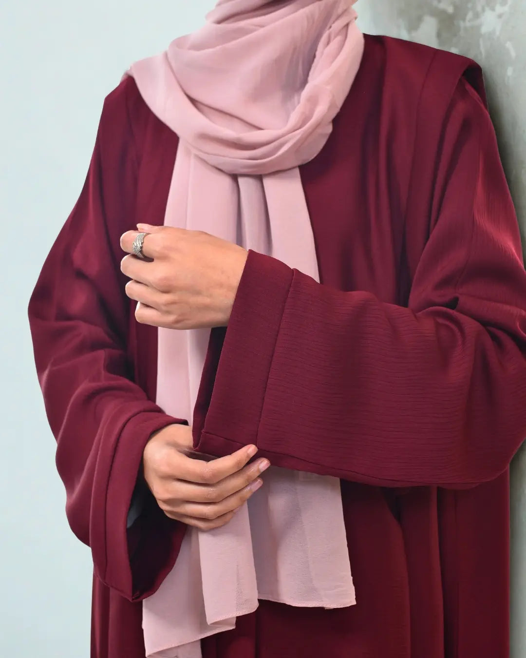 Person wearing a burgundy abaya with a light pink hijab against a light blue background