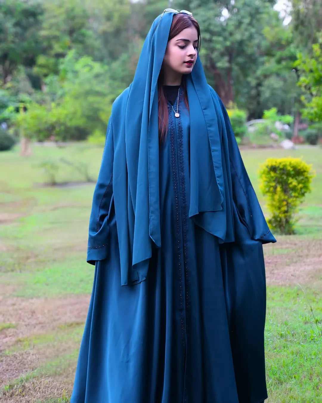 Woman wearing a teal abaya in a park setting