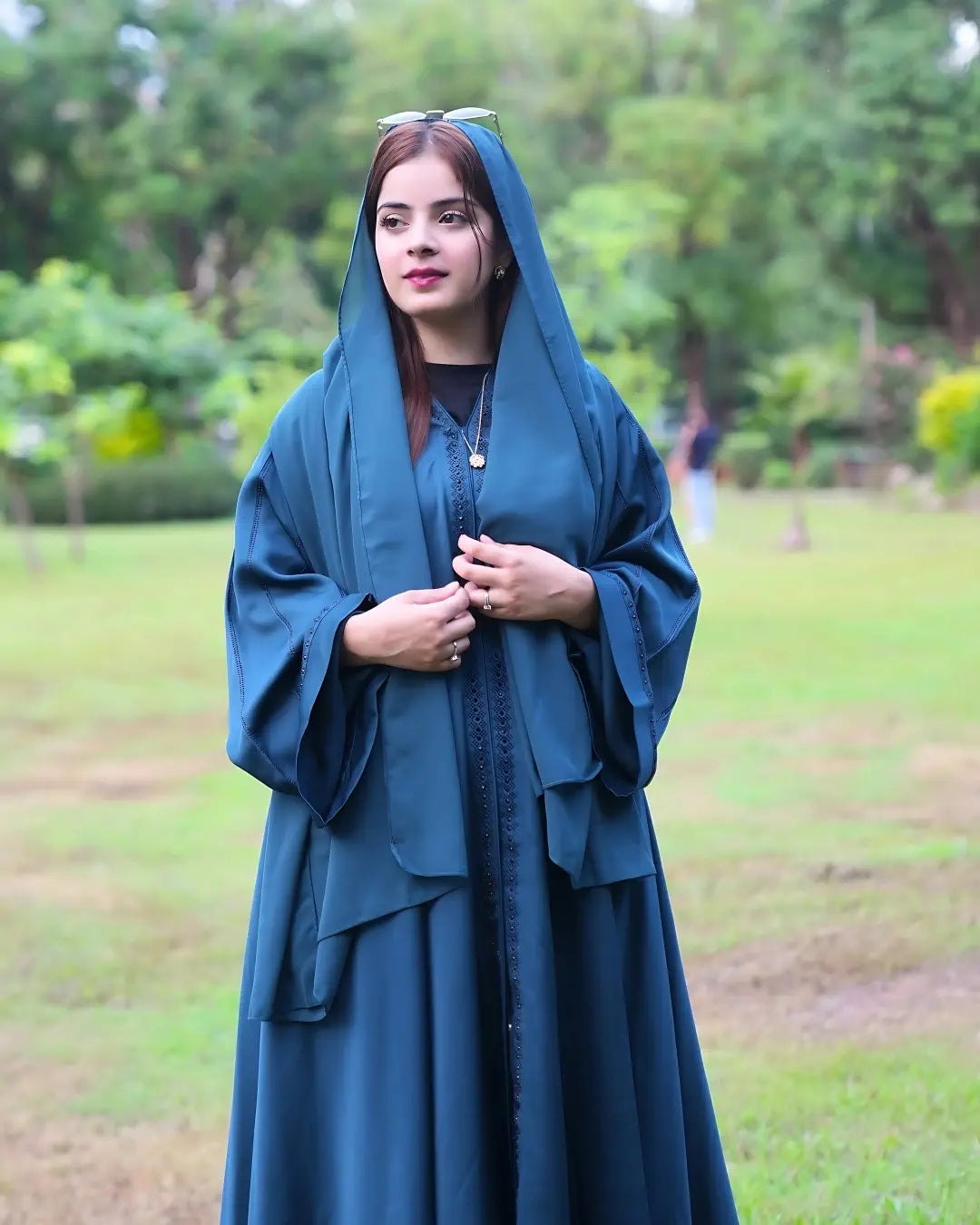 Woman wearing a blue premium abaya standing in a green outdoor setting