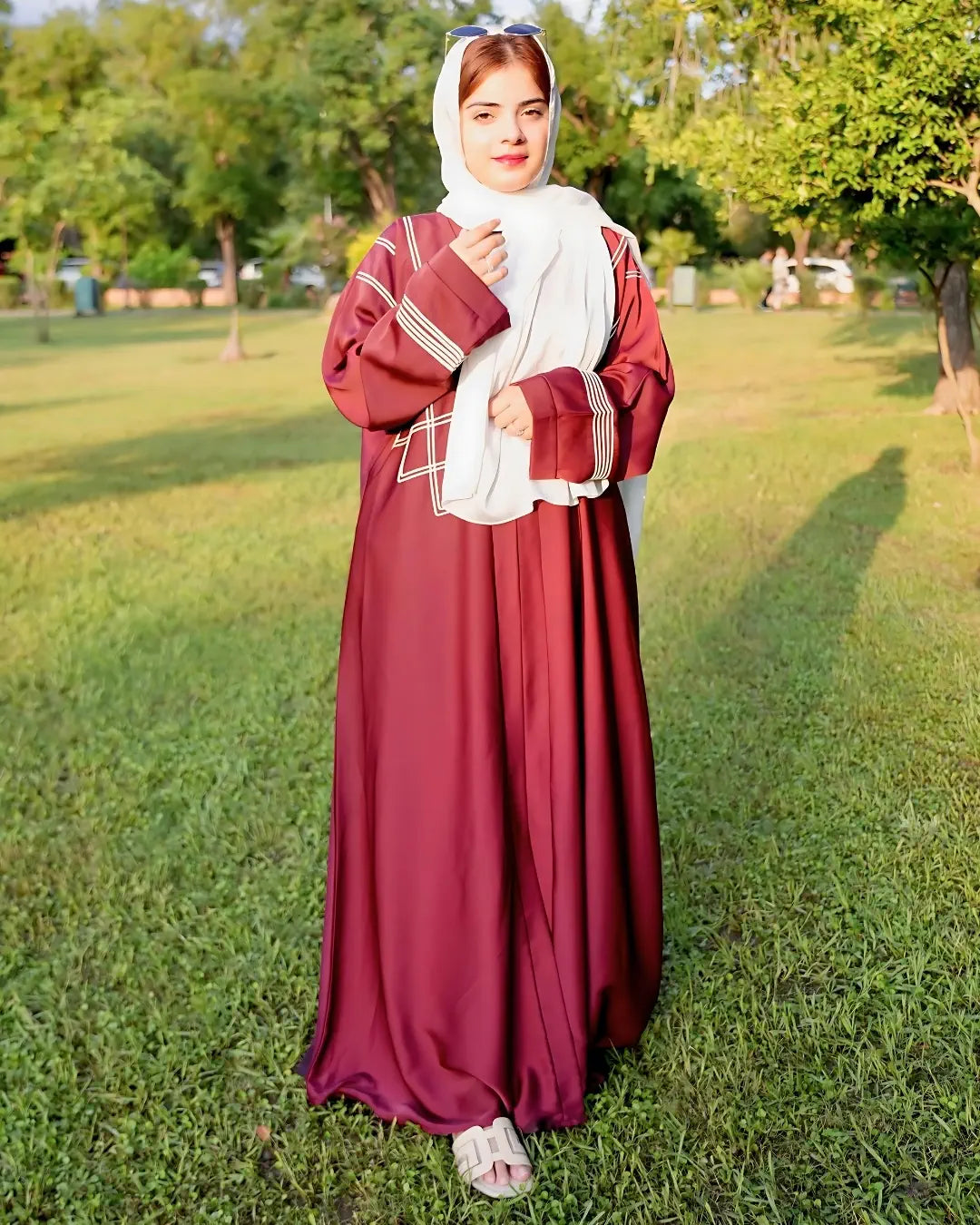 Woman in a burgundy abaya with a white headscarf standing on grass