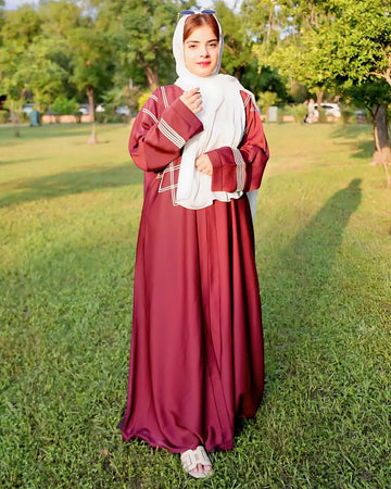 Woman in a burgundy abaya with a white headscarf standing on grass