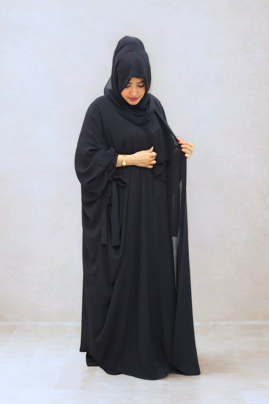 Woman wearing a black abaya against a plain background