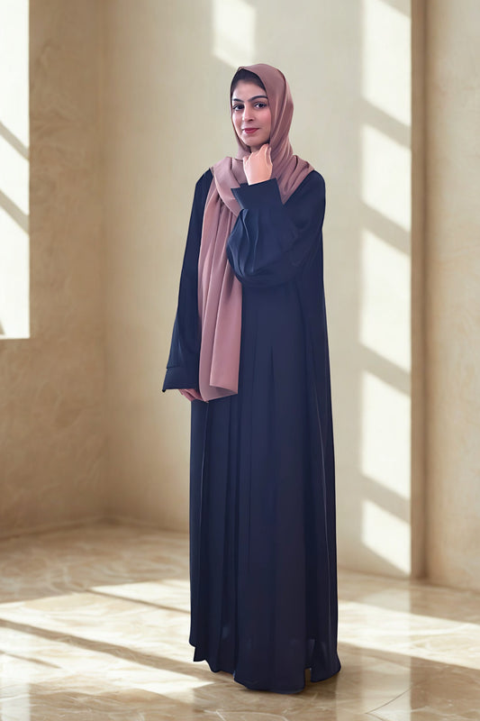 Woman wearing a black abaya with a hijab in a sunlit room.