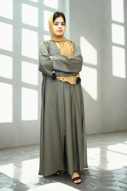 A Girl wearing a Abaya and scarf against a textured wall with sunlight casting shadows.