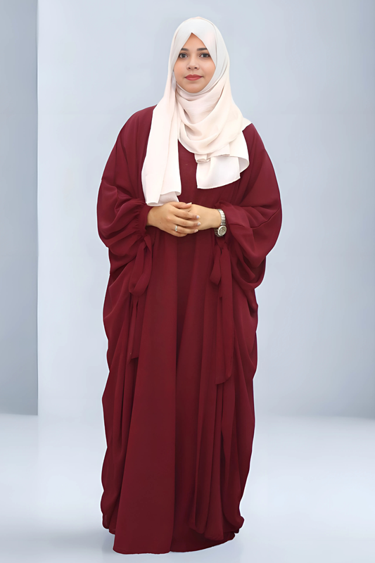 Woman wearing a burgundy abaya with a white hijab on a light gray background