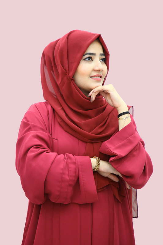 Woman wearing a red hijab and red abaya against a pink background