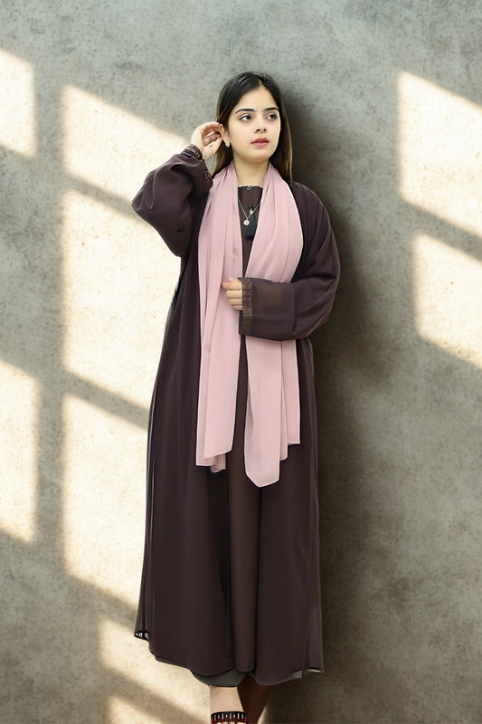 A Girl wearing a Abaya and scarf against a textured wall with sunlight casting shadows.
