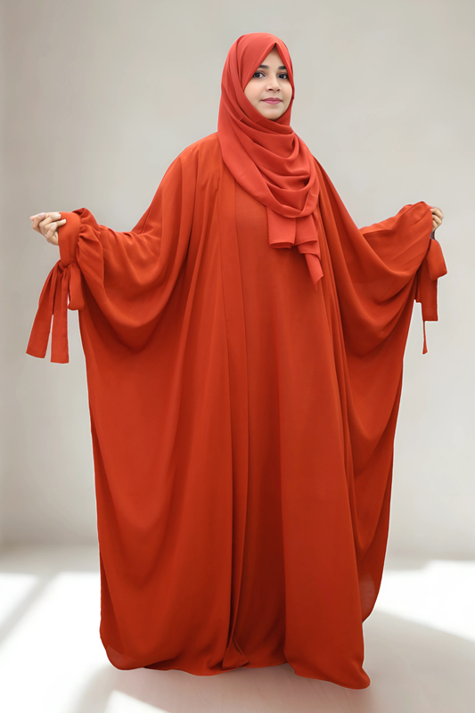 Person wearing a long, flowing orange abaya with a matching headscarf on a plain background