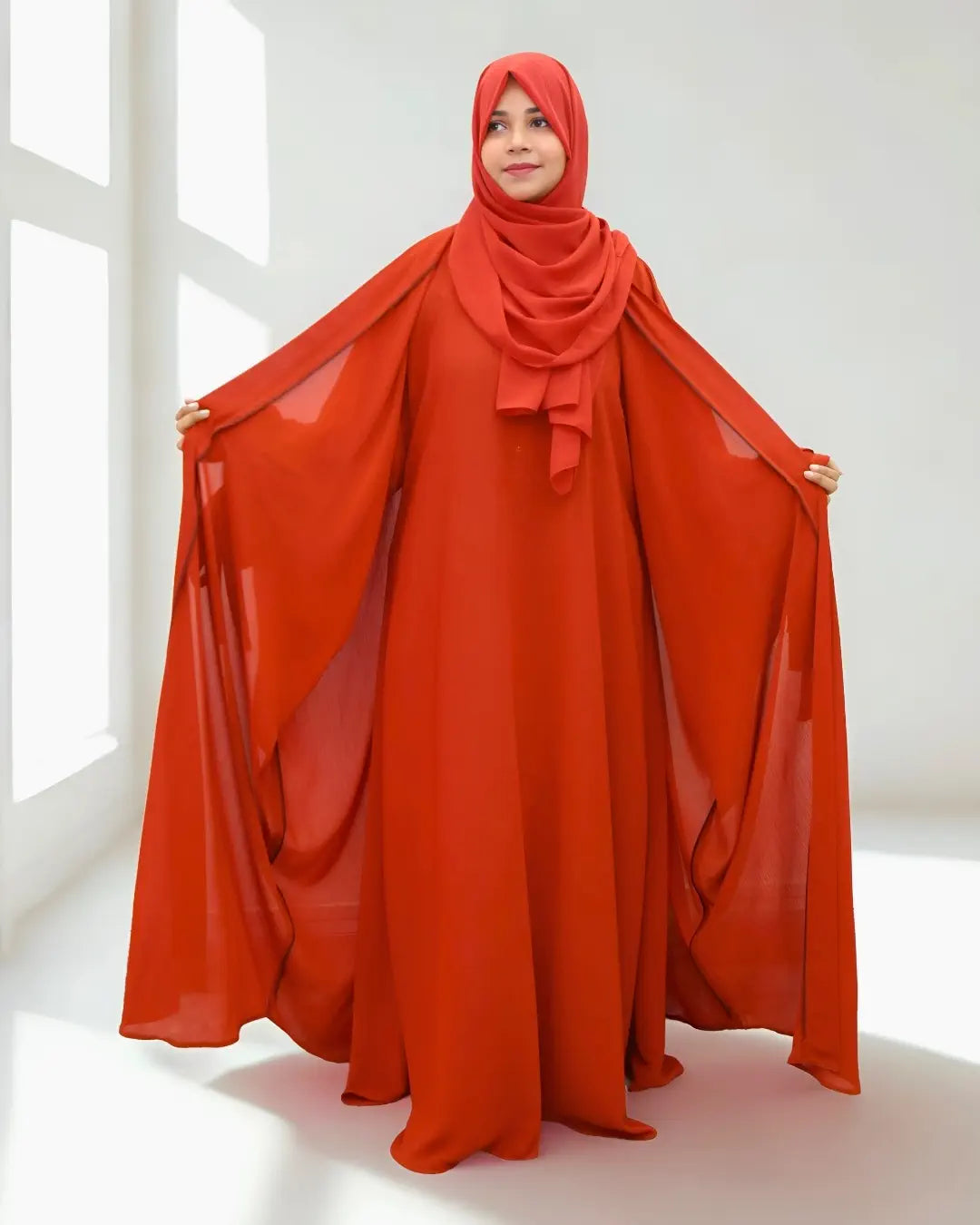 Person wearing a long, flowing orange abaya with a matching hijab in a bright room.