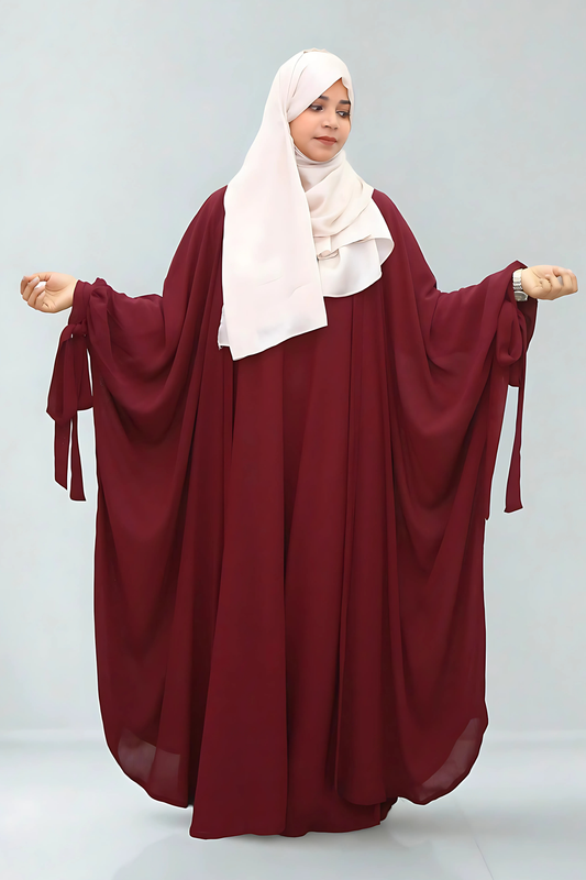 Woman wearing a burgundy abaya with a white hijab on a light gray background