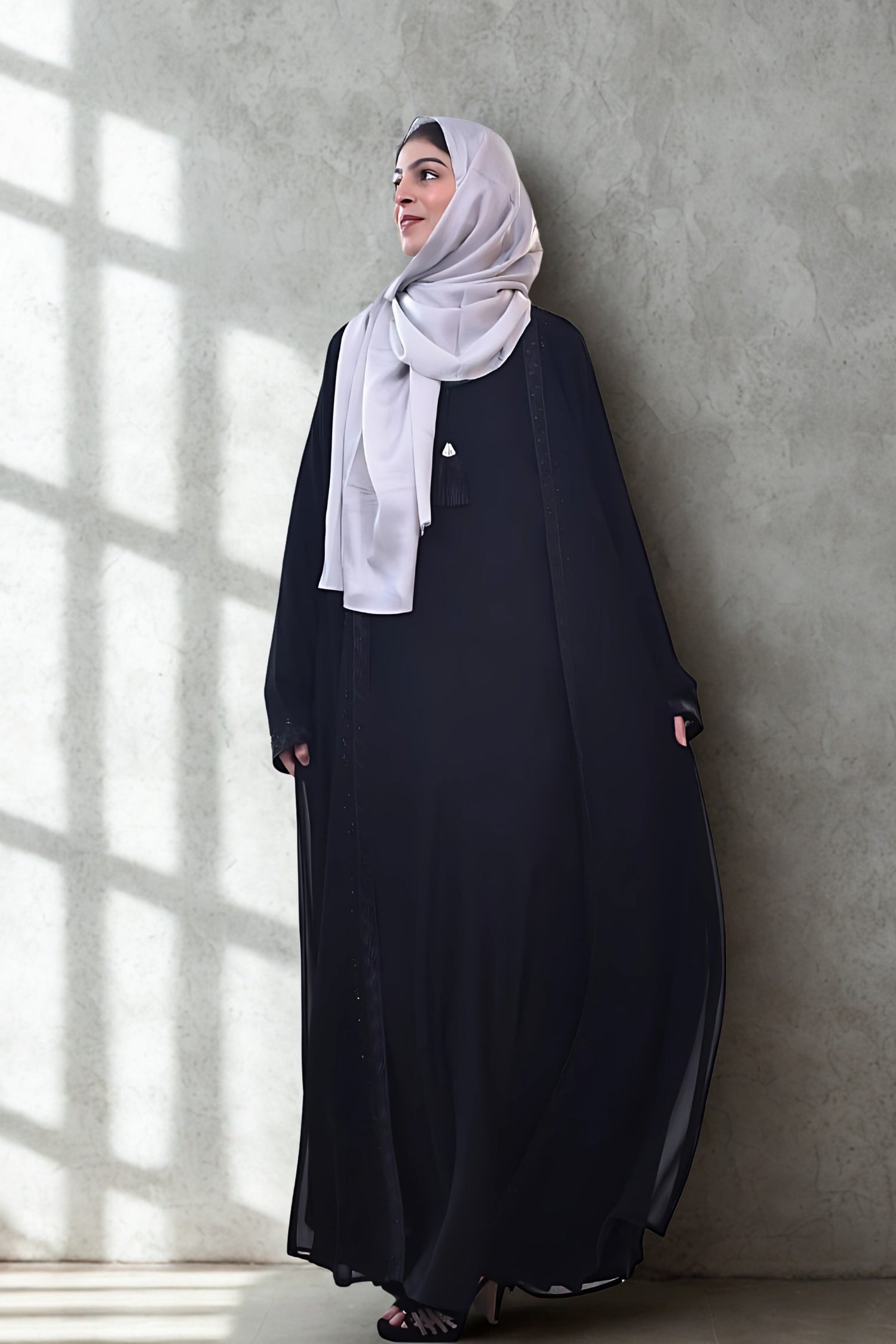 A girl in an Abaya with hijab standing in room with grey background