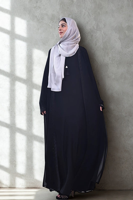 A girl in an Abaya with hijab standing in room with grey background