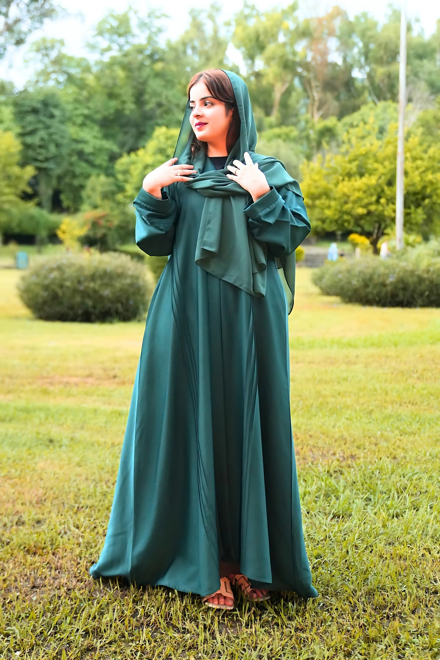 girl wearing a long green dress standing in a grassy area with trees in the background