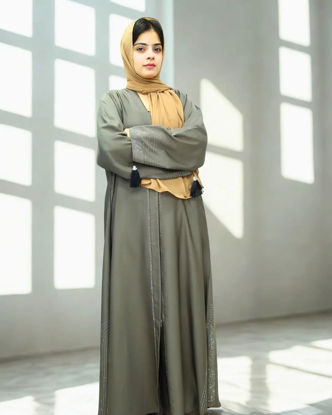 Woman wearing a long green abaya with a beige hijab in a bright room.