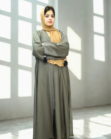 Woman wearing a long green abaya with a beige hijab in a bright room.