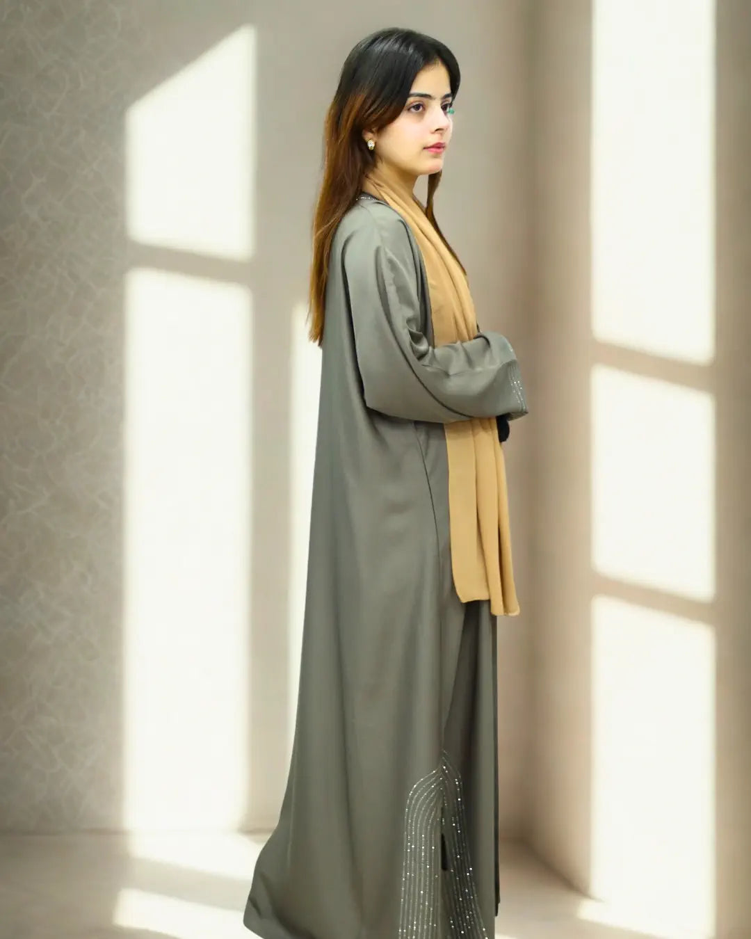 Woman wearing a long green abaya with a yellow scarf standing in a softly lit room.