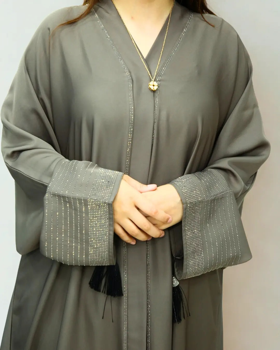 Person wearing a gray abaya with textured cuffs on a plain background