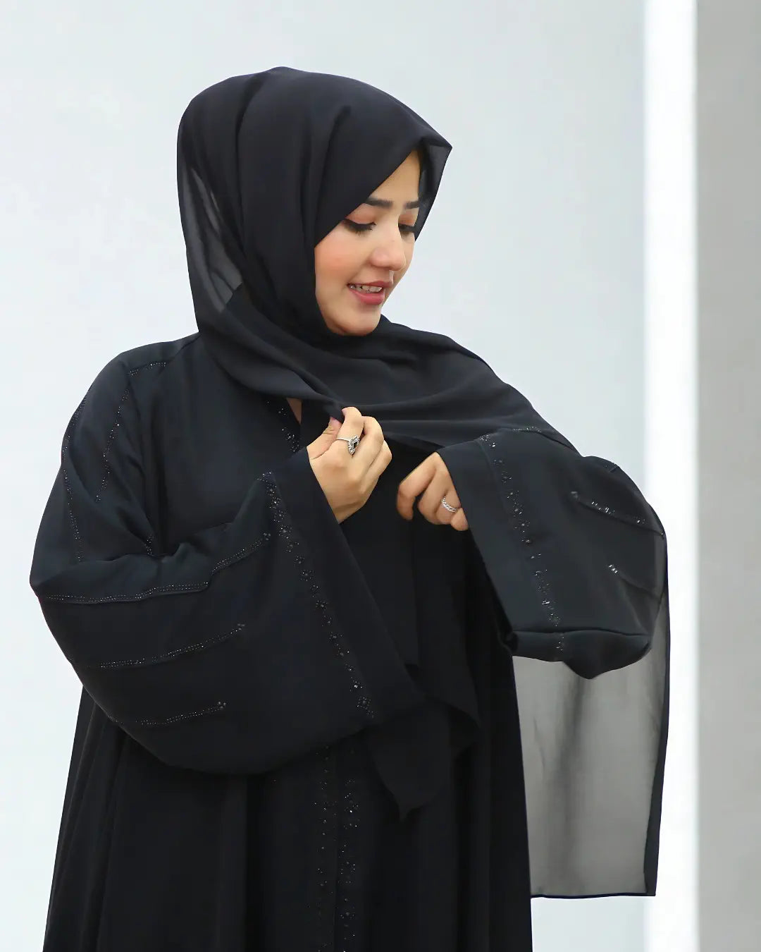 Woman wearing a black abaya and hijab against a white background