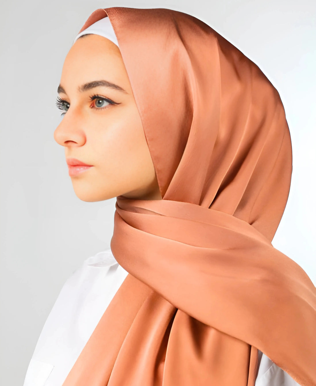 Woman wearing a peach hijab against a light gray background