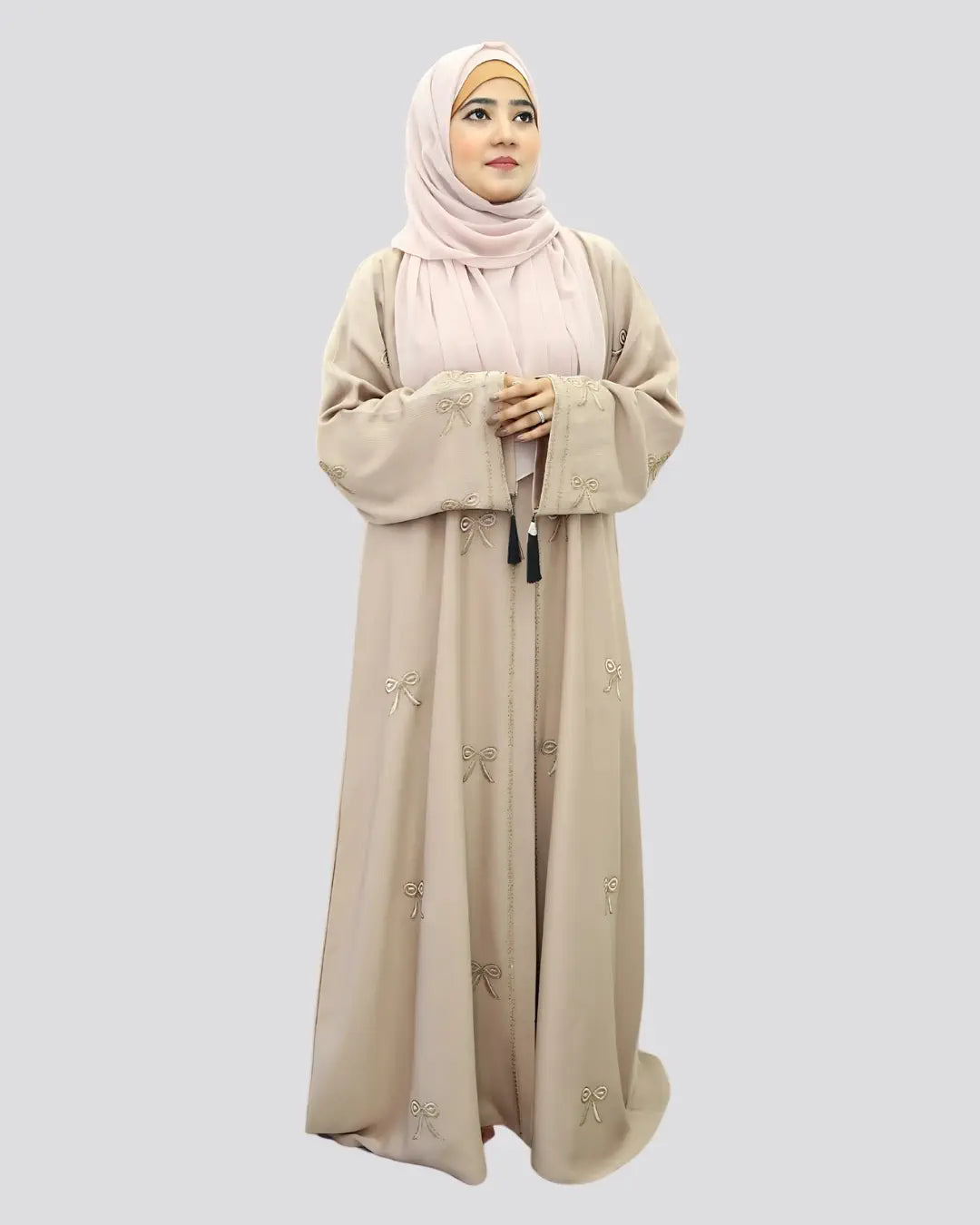 Woman wearing a beige abaya with floral patterns on a light gray background