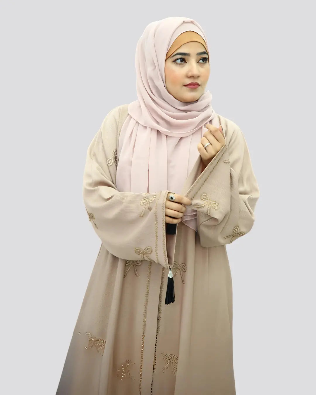 Woman wearing a beige abaya and pink hijab on a light gray background