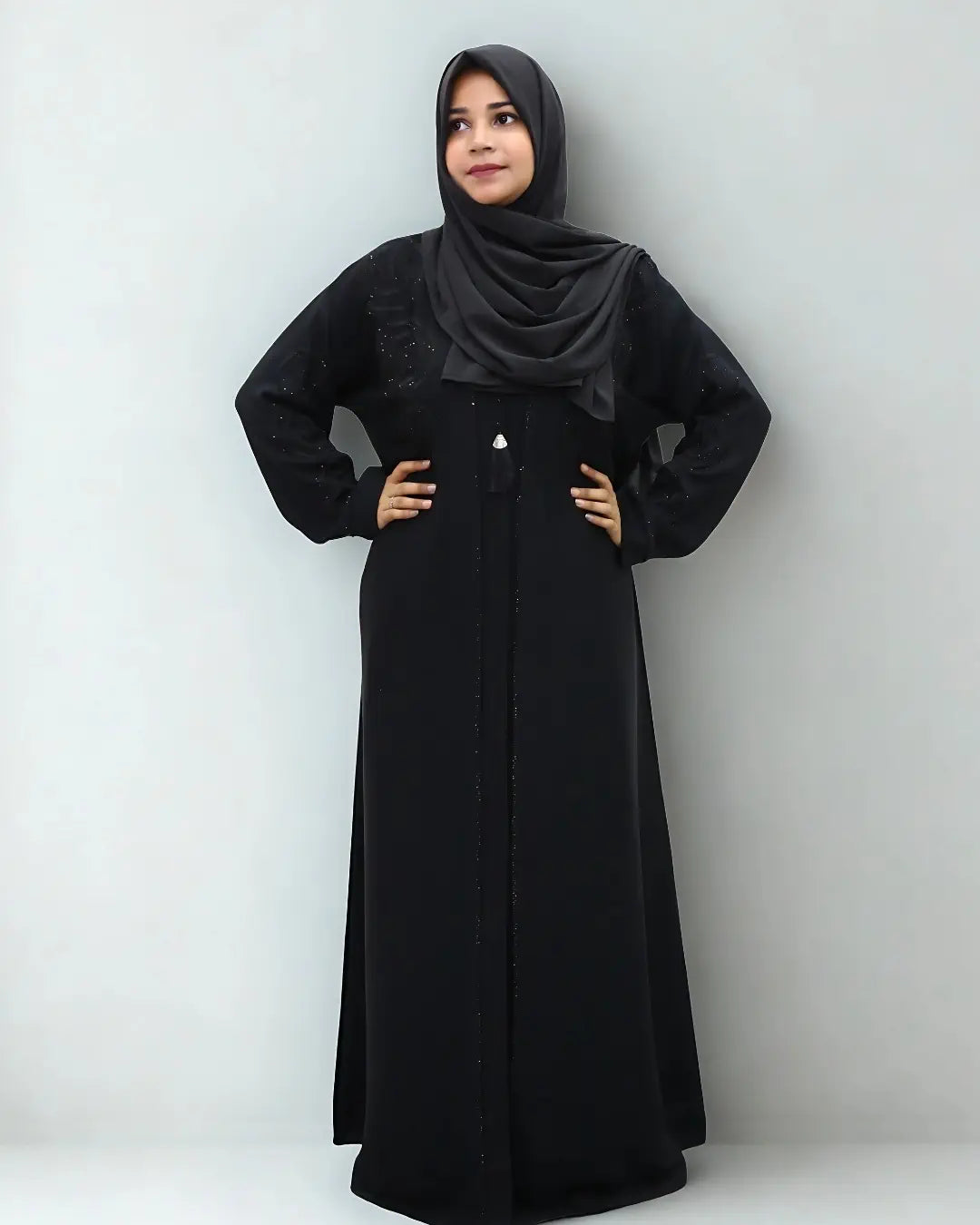 Woman wearing a black abaya and hijab against a white background