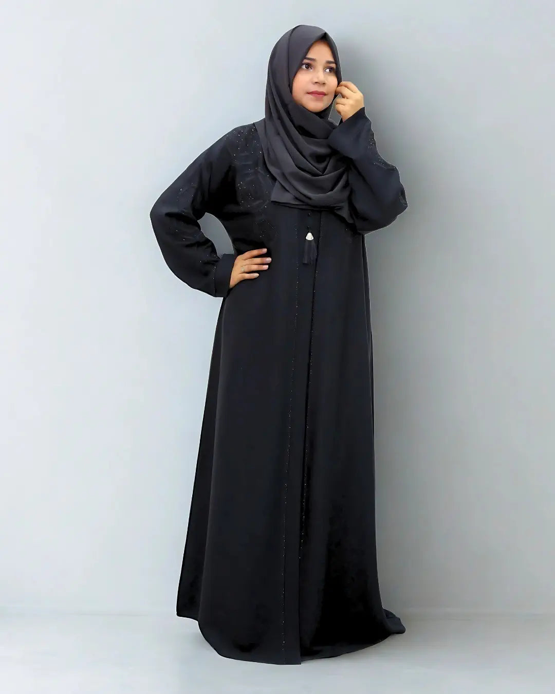 Woman wearing a black abaya and hijab against a plain background