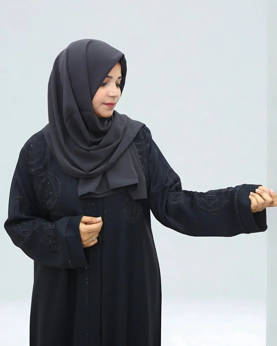 Person wearing a black abaya with a matching hijab against a light gray background