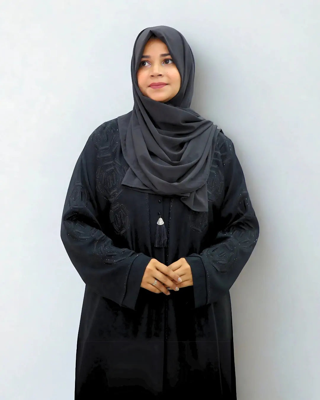 Woman wearing a black abaya and gray hijab against a white background