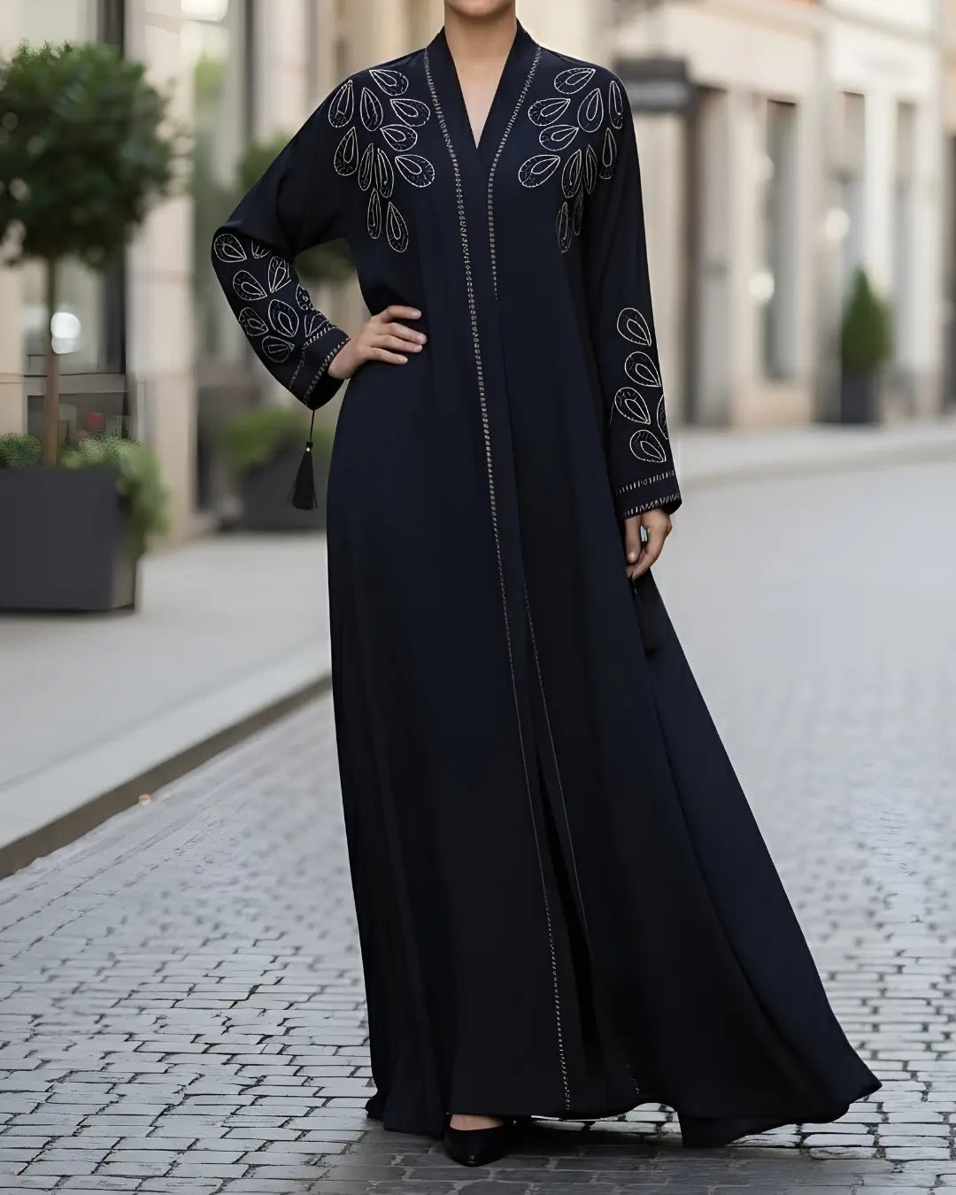 Woman wearing a black abaya with intricate embroidery on a city street.