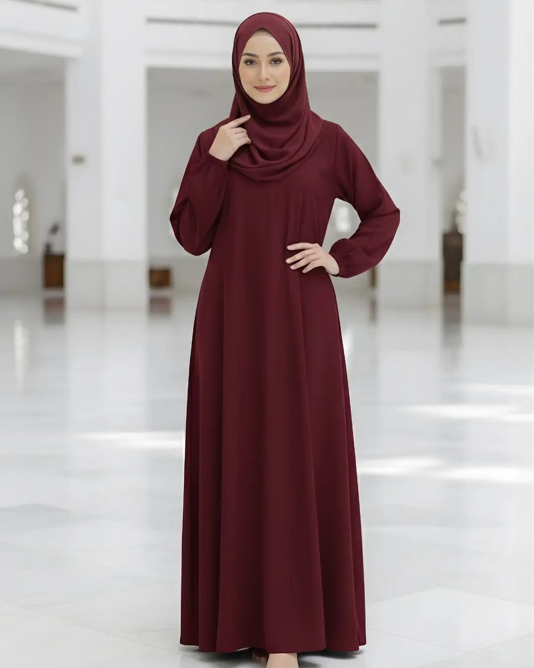 Woman wearing a burgundy Abaya and hijab in a white indoor setting